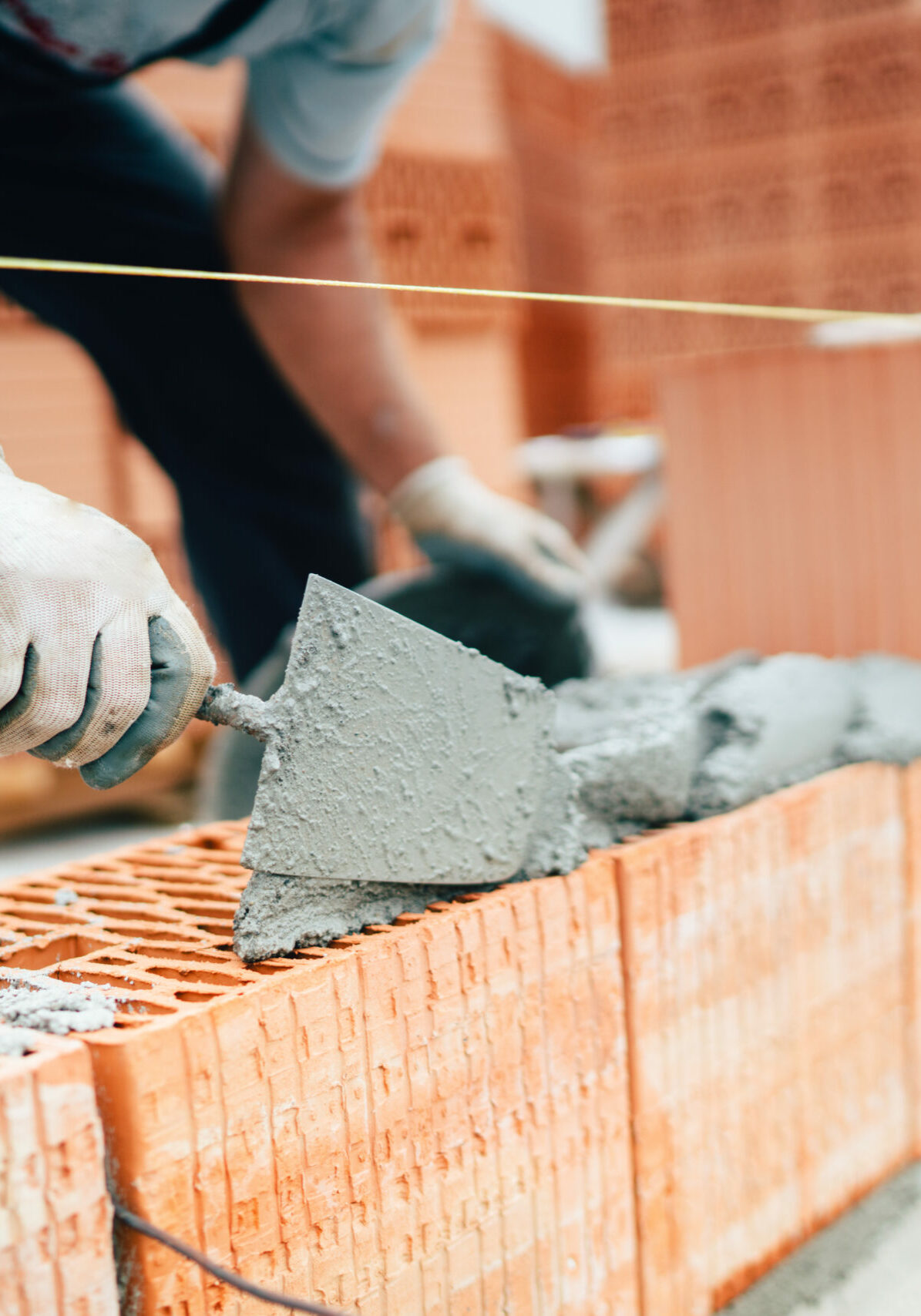 Professional worker using pan knife for building brick walls with cement and mortar